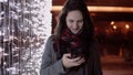 Young attractive woman talking on the phone in the falling snow at Christmas night standing near lights wall, Royalty Free Stock Photo