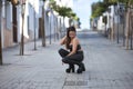 Young and attractive woman, top and leather pants and boots, posing crouched in the middle of a lonely street. Biker concept, Royalty Free Stock Photo