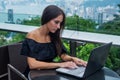 Young attractive woman typing or working on laptop sitting in rooftop cafe with city view.