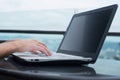 Young attractive woman typing or working on laptop sitting in rooftop cafe with city view.