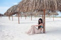 Young attractive woman on vacation at the sea, sitting on the sand under a straw umbrella. Royalty Free Stock Photo