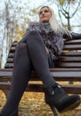A young attractive woman wearing fur black jacket holding book sitting on the bench in falling park. Royalty Free Stock Photo