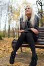 A young attractive woman wearing fur black jacket holding book sitting on the bench in falling park. Royalty Free Stock Photo