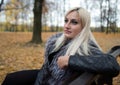 A young attractive woman wearing fur black jacket holding book sitting on the bench in falling park. Royalty Free Stock Photo