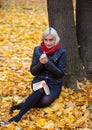 A young attractive woman wearing fur black jacket holding book sitting by the tree. Walking around autumn park. Royalty Free Stock Photo