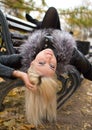 A young attractive woman wearing fur black jacket lying on the bench in falling park. Walking around autumn park. Royalty Free Stock Photo