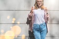 Young attractive woman wearing glasses, white T-shirt, blue jeans, pink denim shirt, stands against a white stone wall. Royalty Free Stock Photo