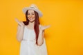 Young attractive woman in a white hat and white summer dress with eco shopping bag smiling on a yellow studio background