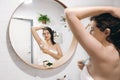 Young attractive woman in white towel shaving armpits, looking in mirror in stylish bathroom. Skin and body care. Hair Removal Royalty Free Stock Photo