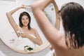 Young attractive woman in white towel shaving armpits with plastic razor after shower, reflection in mirror in stylish bathroom