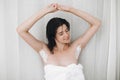 Young attractive woman in white towel sitting and waiting with shaving cream on armpits for depilation, holding hands up in Royalty Free Stock Photo