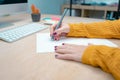 Young attractive woman working from home on her workplace writing on paper with a pen.