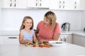 Young attractive woman cooking together with her sweet beautiful blond little 6 or 7 years old daughter smiling happy preparing sa