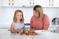 Young attractive woman cooking together with her sweet beautiful blond little 6 or 7 years old daughter smiling happy preparing sa