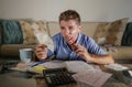Young attractive worried and stressed man at home calculating month tax expenses with calculator accounting payments doing bank pa Royalty Free Stock Photo