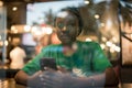 Young authentic black woman sitting with phone in city coffee shop at night