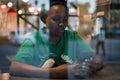 Young authentic black woman sitting with phone in city coffee shop at night