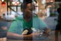 Young authentic black woman sitting with phone in city coffee shop at night