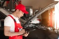 Young auto mechanic with clipboard near car in service center