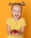 Young baby girl kid hold berries fruits in hands surprised happy laughing screaming on yellow Royalty Free Stock Photo