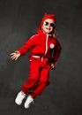 Young baby girl kid jumping in red cloth and sunglasses on dark grey wall Royalty Free Stock Photo