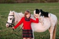 Young baby girl. Red dress. Dog on horseback. Little White Horse pony Royalty Free Stock Photo