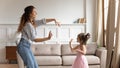 Young babysitter dancing to music with daughter at home.