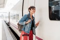 Young backpacker caucasian woman holding luggage at train station ready to catch the train. Holding mobile phone while using app. Royalty Free Stock Photo