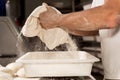 Young baker in bakery shop sprinkling flour with strainer on fresh bread dough in front of oven. concept of traditional manual Royalty Free Stock Photo