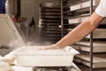Young baker in bakery shop sprinkling flour with strainer on fresh bread dough in front of oven. concept of traditional manual Royalty Free Stock Photo