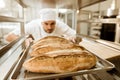 young baker putting trays of fresh bread on stand