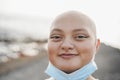 Young bald girl smiling on camera with safety mask under chin outdoor in the city - Focus on face Royalty Free Stock Photo