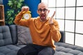 Young bald man with beard holding alarm clock celebrating victory with happy smile and winner expression with raised hands Royalty Free Stock Photo