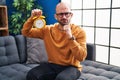 Young bald man with beard holding alarm clock serious face thinking about question with hand on chin, thoughtful about confusing Royalty Free Stock Photo