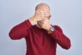 Young bald man with beard standing over white background wearing glasses covering eyes and mouth with hands, surprised and shocked Royalty Free Stock Photo