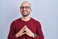 Young bald man with beard standing over white background wearing glasses hands together and fingers crossed smiling relaxed and Royalty Free Stock Photo