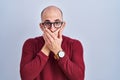 Young bald man with beard standing over white background wearing glasses shocked covering mouth with hands for mistake Royalty Free Stock Photo