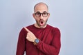 Young bald man with beard standing over white background wearing glasses surprised pointing with finger to the side, open mouth Royalty Free Stock Photo