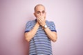 Young bald man with beard wearing casual striped blue t-shirt over pink isolated background shocked covering mouth with hands for Royalty Free Stock Photo