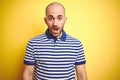 Young bald man with beard wearing casual striped blue t-shirt over yellow isolated background afraid and shocked with surprise Royalty Free Stock Photo