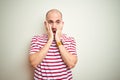 Young bald man with beard wearing casual striped red t-shirt over white isolated background afraid and shocked, surprise and Royalty Free Stock Photo
