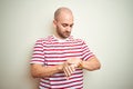 Young bald man with beard wearing casual striped red t-shirt over white isolated background Checking the time on wrist watch,