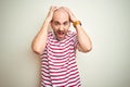 Young bald man with beard wearing casual striped red t-shirt over white isolated background Crazy and scared with hands on head, Royalty Free Stock Photo