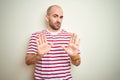 Young bald man with beard wearing casual striped red t-shirt over white isolated background Moving away hands palms showing Royalty Free Stock Photo