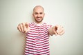 Young bald man with beard wearing casual striped red t-shirt over white isolated background pointing to you and the camera with Royalty Free Stock Photo