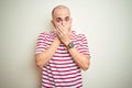Young bald man with beard wearing casual striped red t-shirt over white isolated background shocked covering mouth with hands for Royalty Free Stock Photo