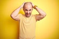 Young bald man with beard wearing casual striped t-shirt over yellow isolated background Crazy and scared with hands on head, Royalty Free Stock Photo