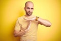 Young bald man with beard wearing casual striped t-shirt over yellow isolated background Doing time out gesture with hands, Royalty Free Stock Photo