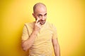 Young bald man with beard wearing casual striped t-shirt over yellow isolated background Pointing to the eye watching you gesture, Royalty Free Stock Photo