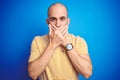 Young bald man with beard wearing casual t-shirt over blue isolated background shocked covering mouth with hands for mistake Royalty Free Stock Photo